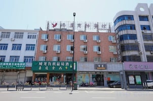 Un edificio de varios pisos con una hilera de comercios en la planta baja, incluyendo un letrero verde para un restaurante y uno morado para una tienda.