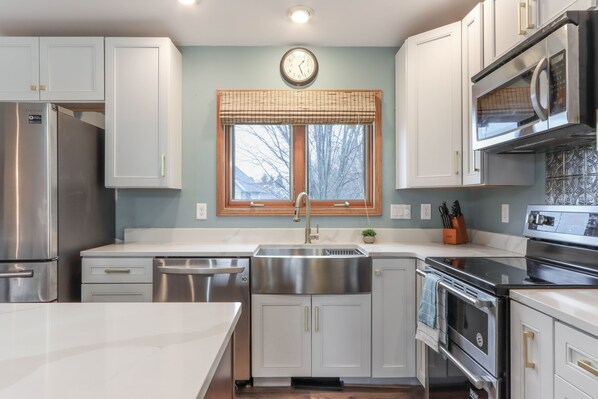 A modern kitchen with stainless steel appliances, white cabinetry, a large window with a view, and a clock on the wall. - 3-bed, 3-bath, 3-car garage executive home in Marshfield, WI (Marshfield)