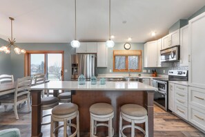 A modern kitchen with a large island, stainless steel appliances, and a dining area with a view. - 3-bed, 3-bath, 3-car garage executive home in Marshfield, WI (Marshfield)