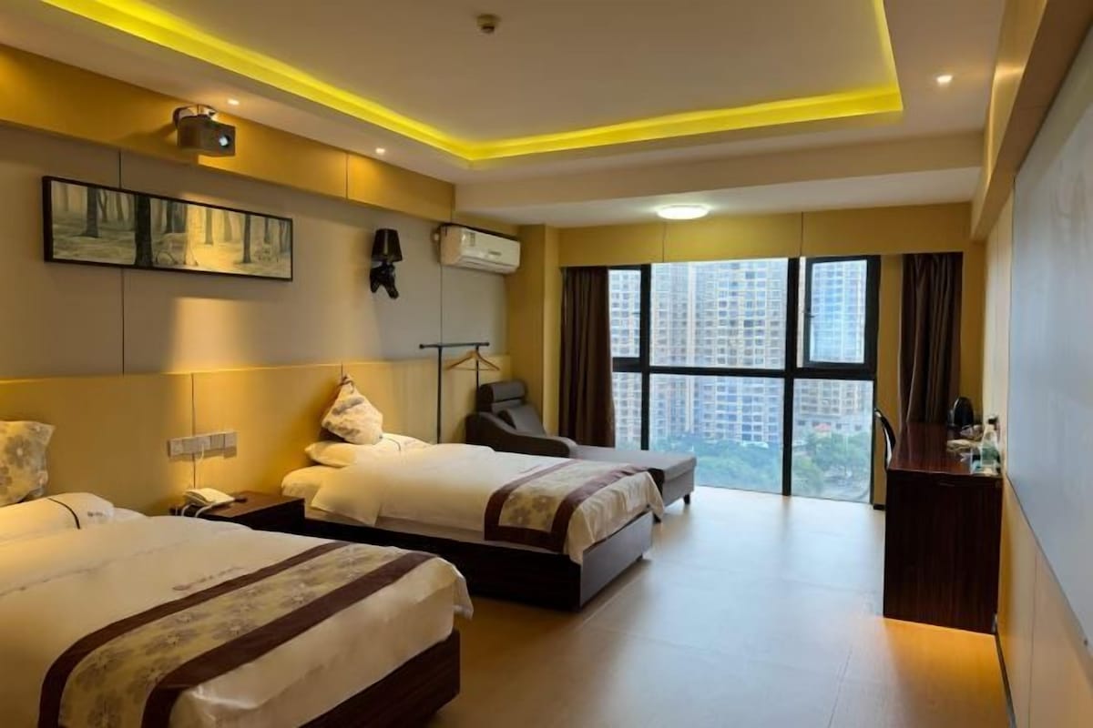 A hotel room with two beds, a desk, and a large window with a city view.