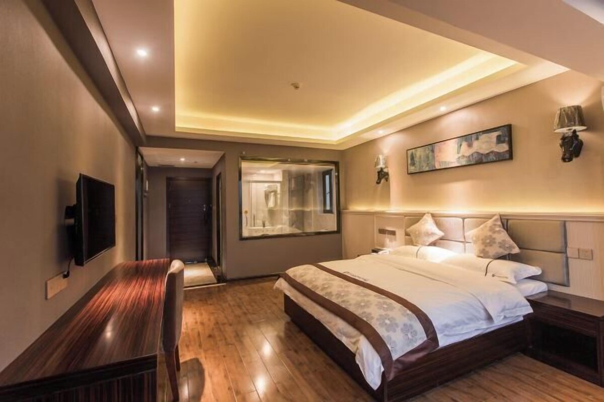 A hotel room with a bed, a desk, a TV, and a painting on the wall.