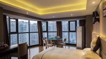 A hotel room with a bed, a desk with a chair, a pool table, and large windows offering a city view.
