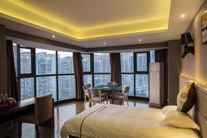 A hotel room with a bed, a desk with a chair, a pool table, and large windows offering a city view. - Cangzhou Maiji Fashion Chain Hotel (Chenzhou)