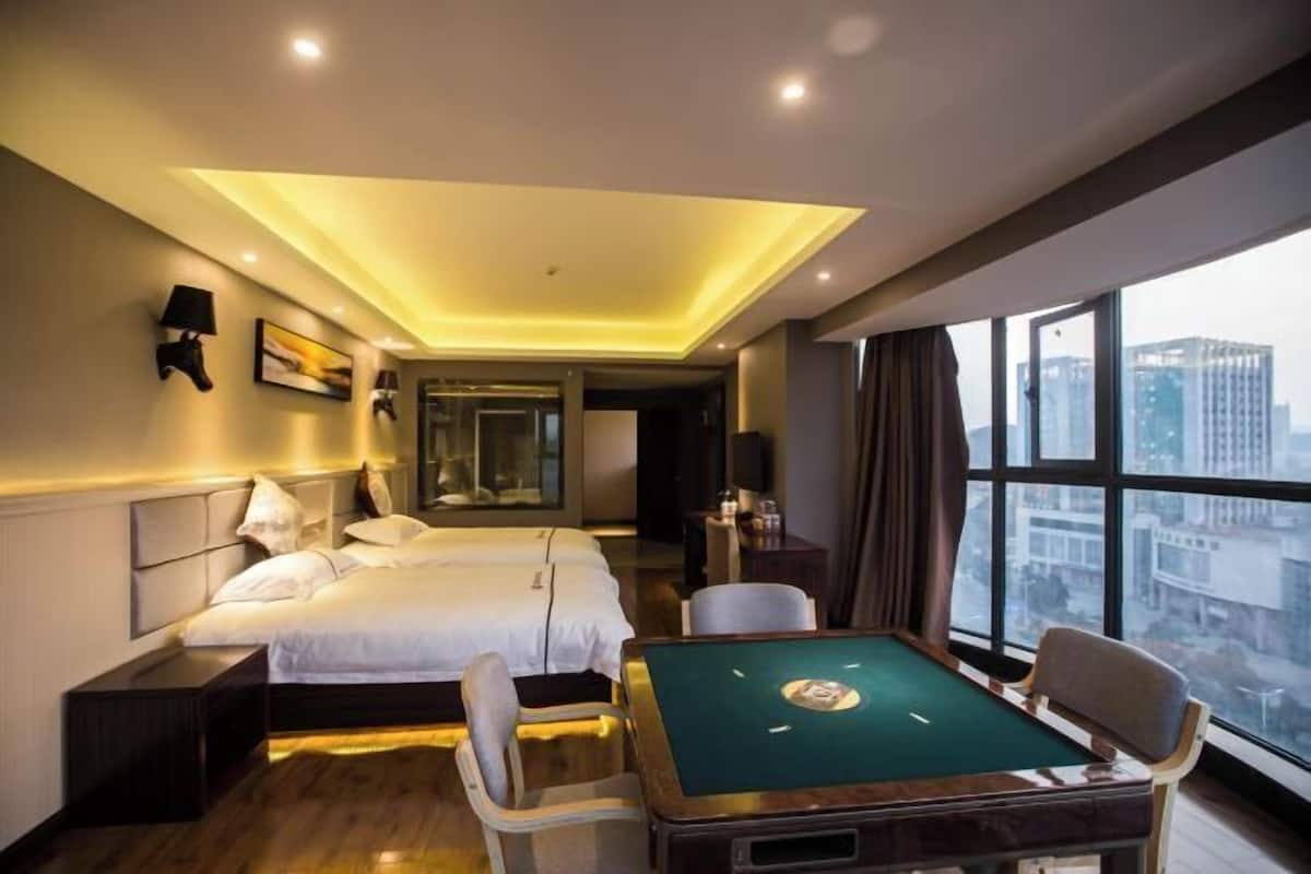 A hotel room with a bed, a pool table, and a large window offering a city view.