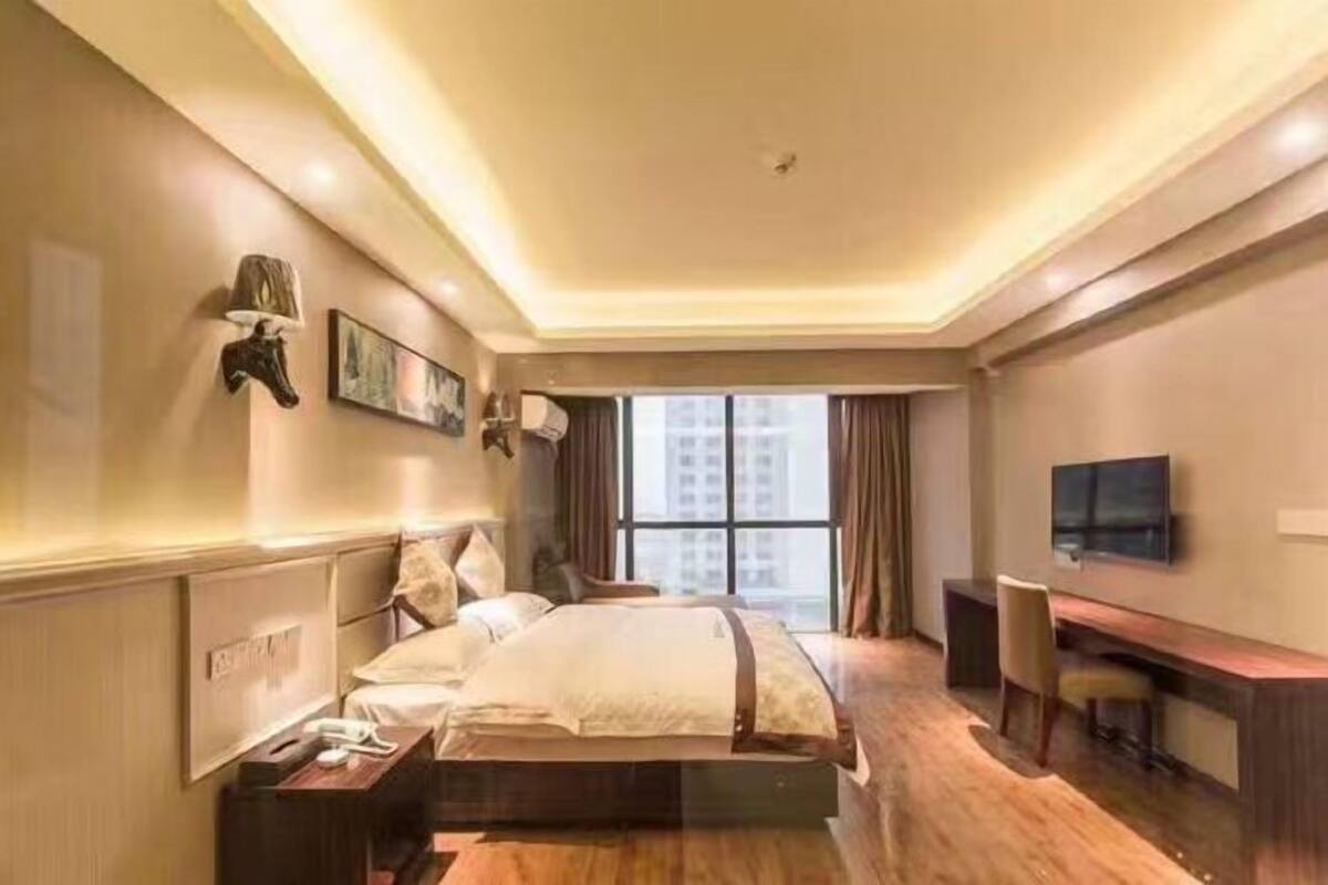 A hotel room with a bed, bedside table, lamp, TV, and a desk with a chair.