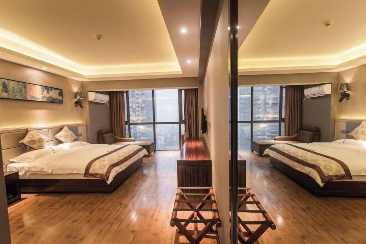 A hotel room with two beds, a wooden floor, a large window, and a view of the city.