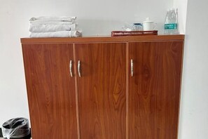 A wooden wardrobe with two doors, a stack of white towels, a red book, a white teapot, and a water bottle on top. - Cangzhou Maiji Fashion Chain Hotel (Chenzhou)