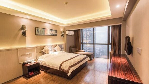 A modern hotel room with a large bed, a seating area, a flat-screen TV, and a large window with a city view. - Cangzhou Maiji Fashion Chain Hotel (Chenzhou)
