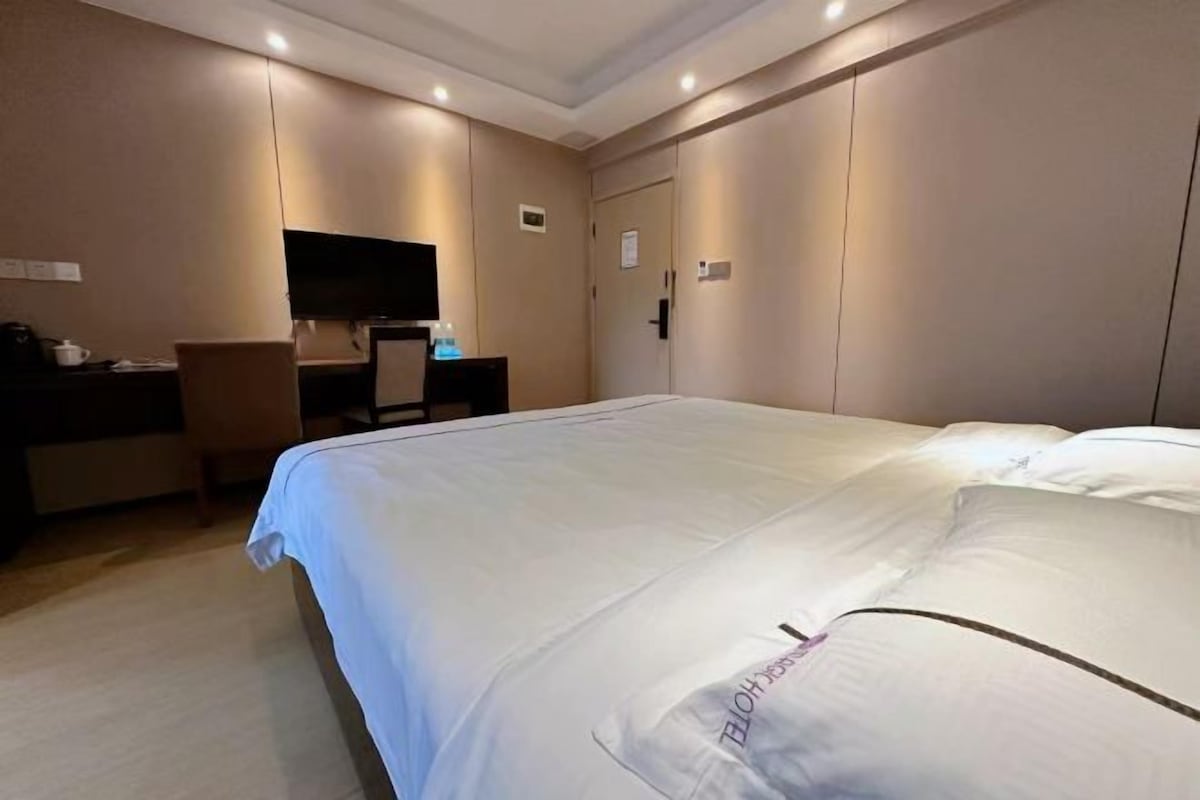 A hotel room with a large bed, a desk with a chair, a television, and a wardrobe.