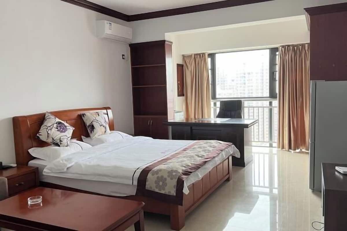 A hotel room with a bed, a desk, a chair, a TV, and a window with curtains.
