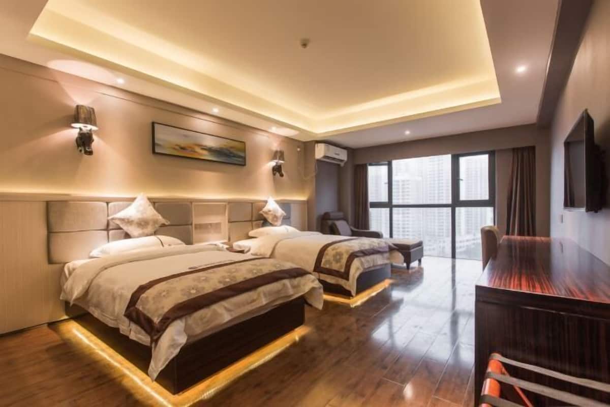 A hotel room with two beds, a desk, and a large window.