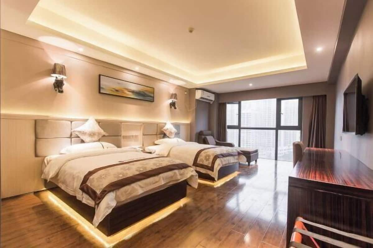 A hotel room with two beds, a desk, a chair, and a large window.