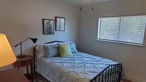 A bedroom with a bed, a lamp, two framed pictures on the wall, and a window with blinds. - DT Boise Townhome near BSU (Boise)