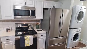 A kitchen with white cabinets, a stainless steel refrigerator, a microwave, an oven, and a washing machine. - DT Boise Townhome near BSU (Boise)
