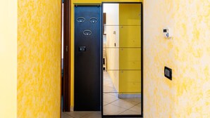 Ein Korridor mit gelber Wand, einer schwarzen Tür mit Spiegel und einem gelben Schrank mit Schubladen.