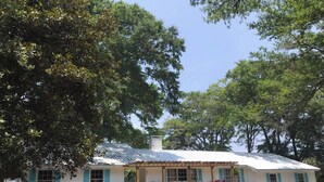 A white building with blue shutters, a porch with chairs, and a gravel driveway.
