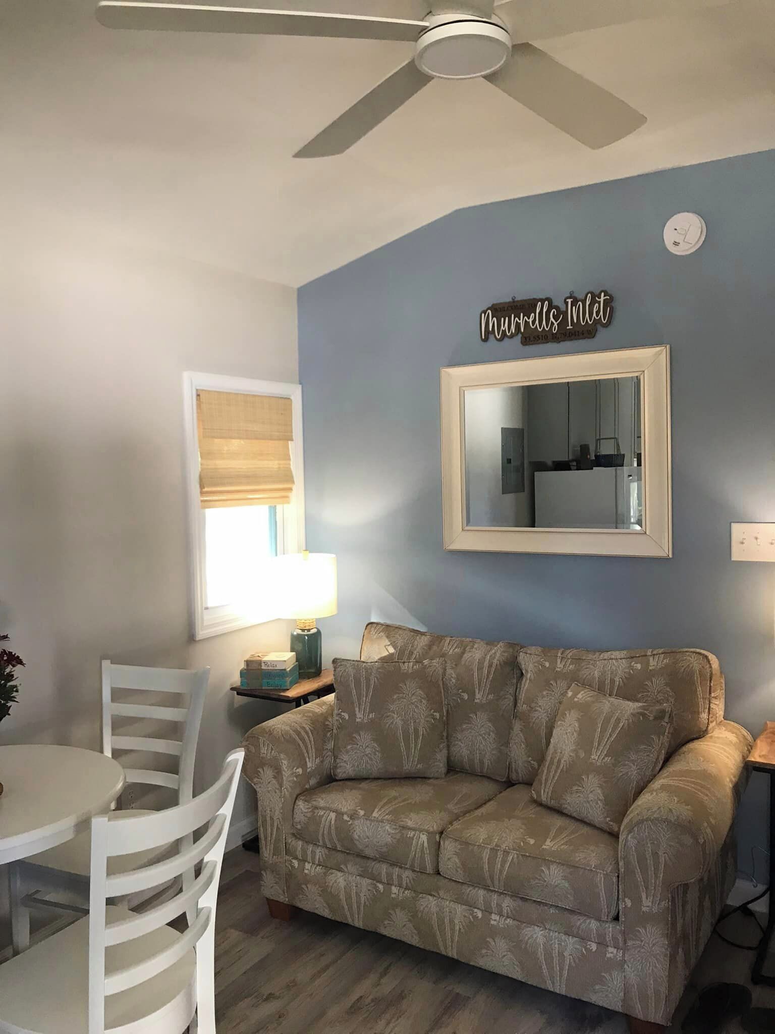 A living room with a blue wall, a ceiling fan, a sofa, a dining table with chairs, and a mirror.