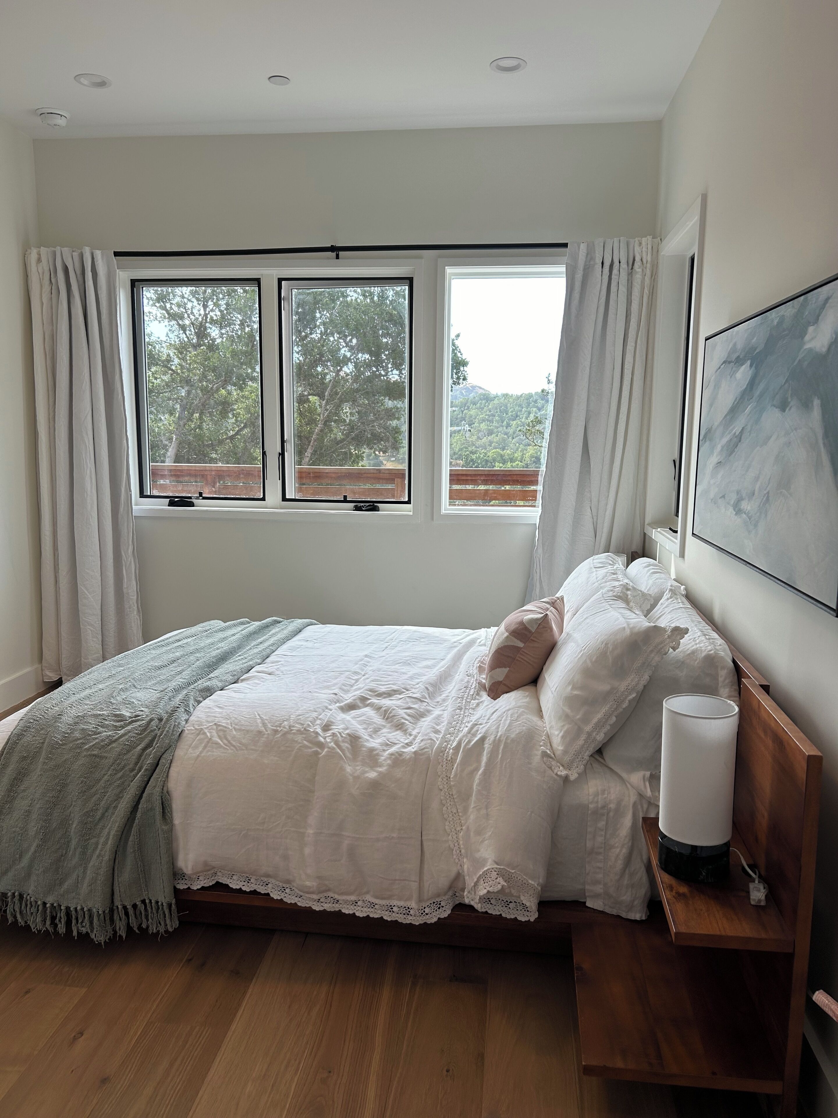 A bedroom with a bed, a bedside table, a lamp, and two windows with curtains.