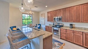 A kitchen with a granite countertop, stainless steel appliances, wooden cabinets, and a bar area with wicker chairs. - Beautifully RENOVATED 3 Bed/2.5 Bath Condo with ALL King beds in Ole at Lely!  (Naples)