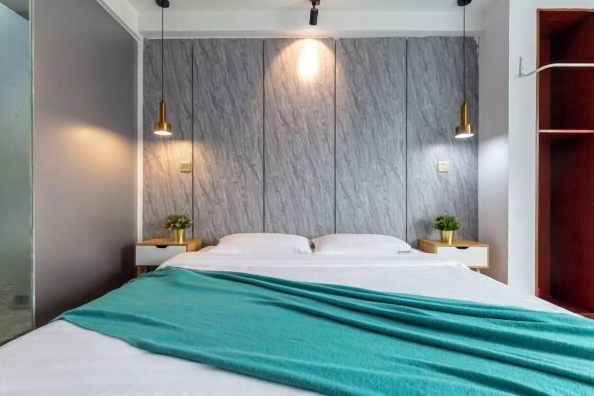 A modern bedroom with a large bed, two bedside tables with lamps, a marble-patterned headboard, and a teal throw blanket.