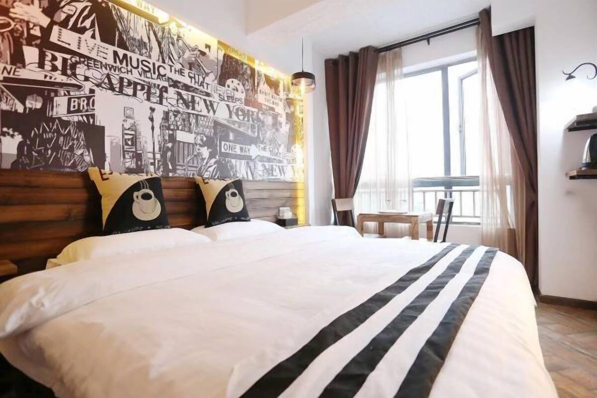 A hotel room with a large bed, a wall mural, a window with curtains, and a small table.