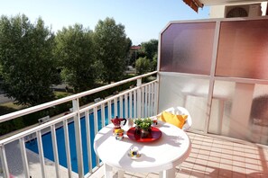 A balcony with a white table, a red tray, a coffee maker, and a potted plant. - 5-person Caorle Apartment With Pool (Caorle)