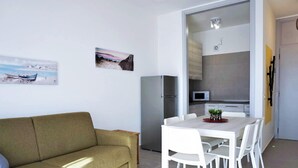 Una sala de estar moderna con un sofá, una mesa de comedor con sillas y una cocina con refrigerador y microondas.