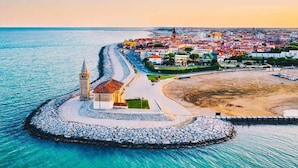 Un pueblo costero con una iglesia destacada, una playa de arena y un rompeolas rocoso.