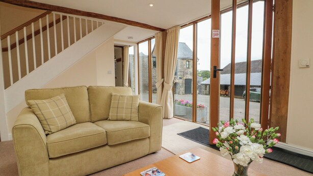 A living room with a beige sofa, a wooden coffee table, and a vase with flowers. - Hunstone Barn (South Molton)