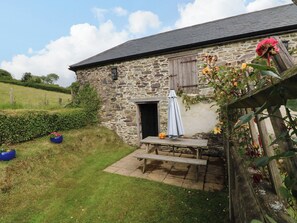 A stone building with a wooden bench and a table under a covered area. - Hunstone Barn (South Molton)