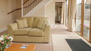 A living room with a beige sofa, a wooden coffee table, and a view through a large window. - Hunstone Barn (South Molton)