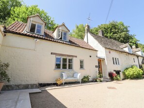 Un bâtiment traditionnel à deux étages, doté d’un toit en tuiles, d’un petit porche avec un banc et d’une enseigne indiquant « Spring Cottage ».