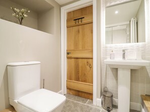Une salle de bain avec des toilettes blanches, une porte en bois et un lavabo surmonté d’un miroir.