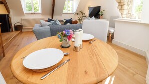 Ein Essbereich mit einem runden Holztisch, gedeckt für zwei Personen, einer Blumenvase und einer Steinwand im Hintergrund.