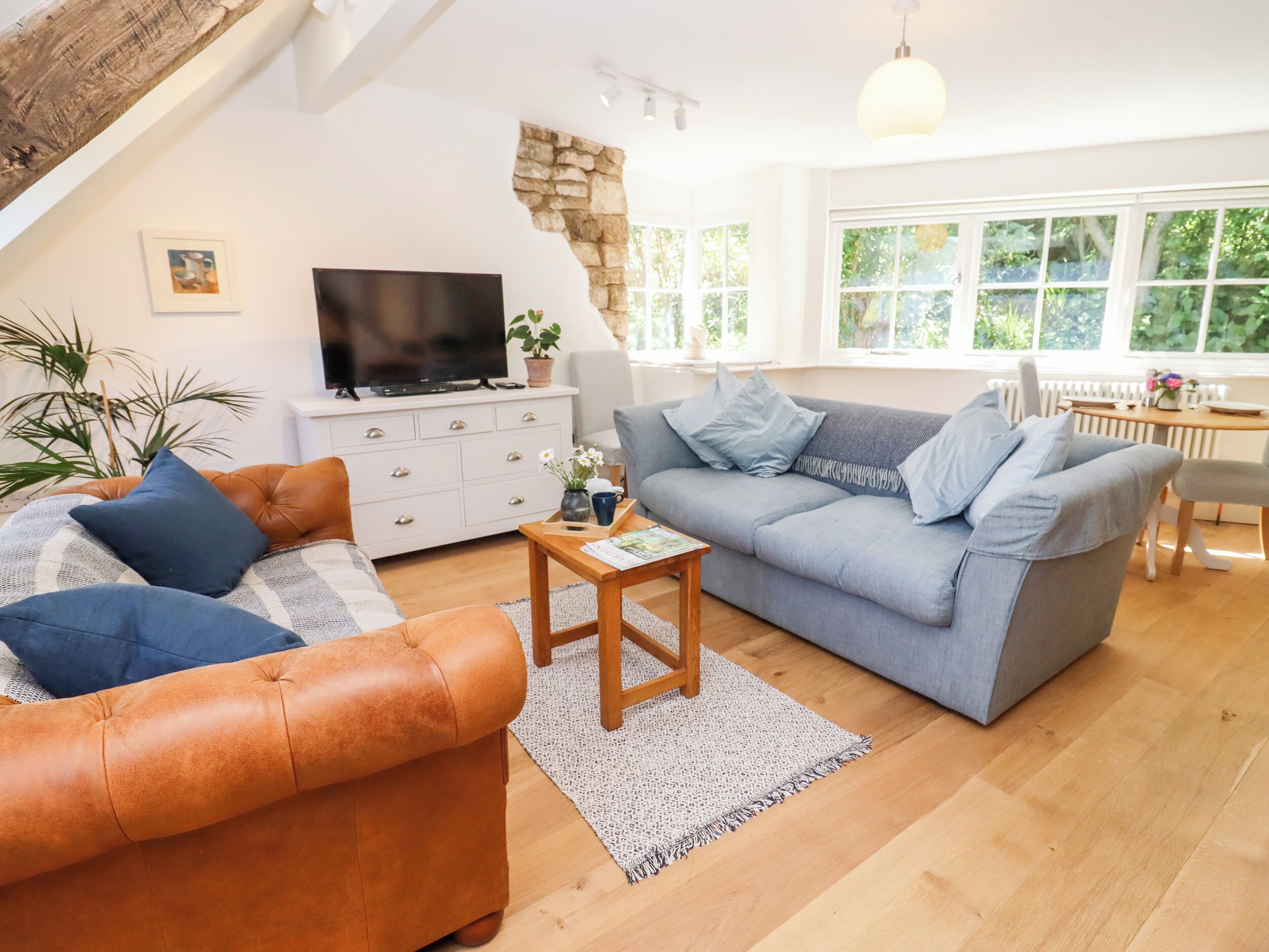 A cozy living room with a loft-style ceiling, a grey sofa, a brown leather couch, a wooden coffee table, and a TV on a white cabinet.