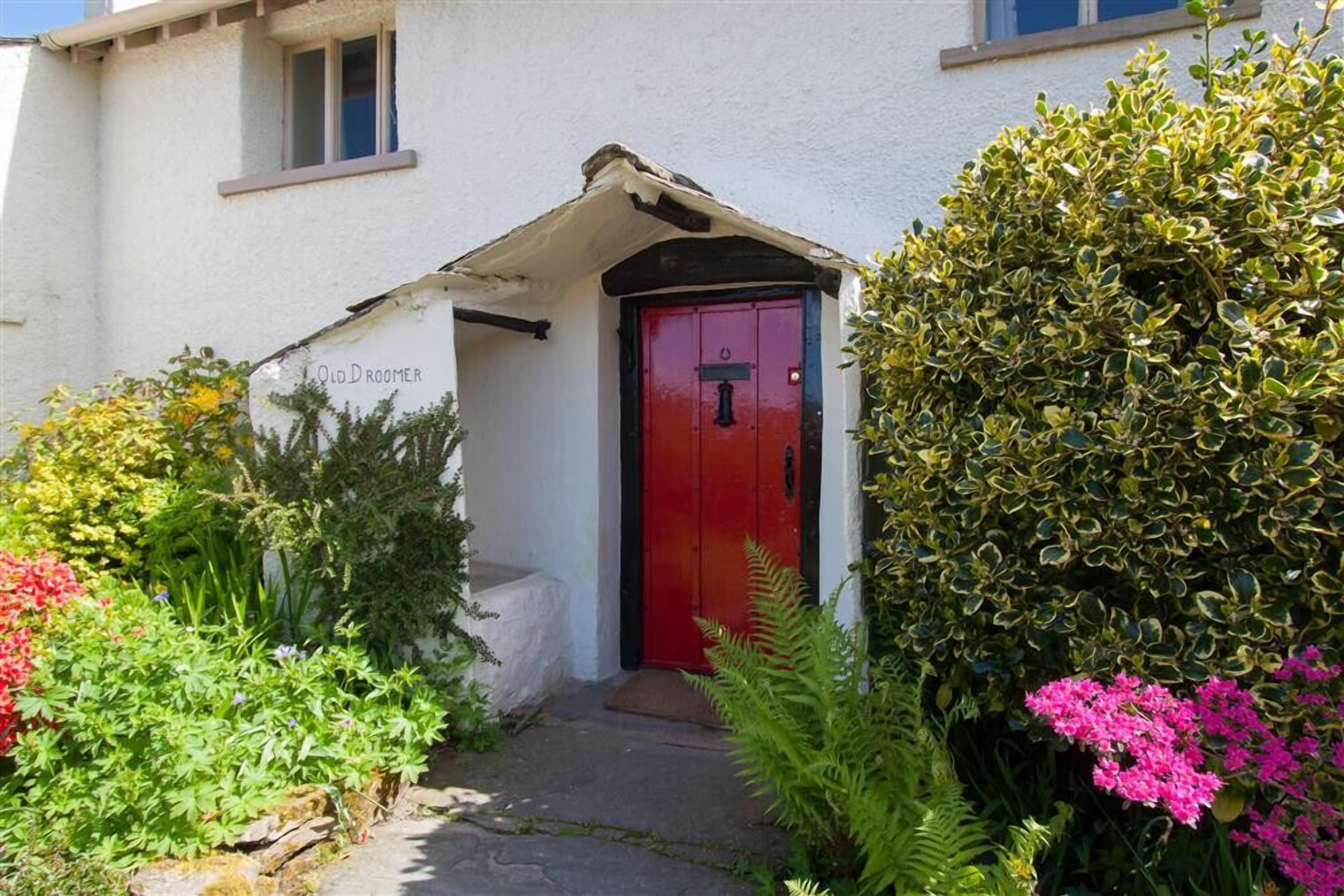 A building with a red door, white walls, and a small garden with various plants and flowers.