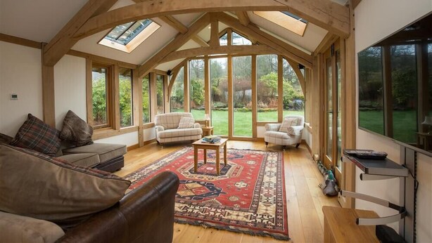 Une pièce spacieuse avec des poutres en bois, de grandes fenêtres, un tapis rouge à motifs et un canapé.