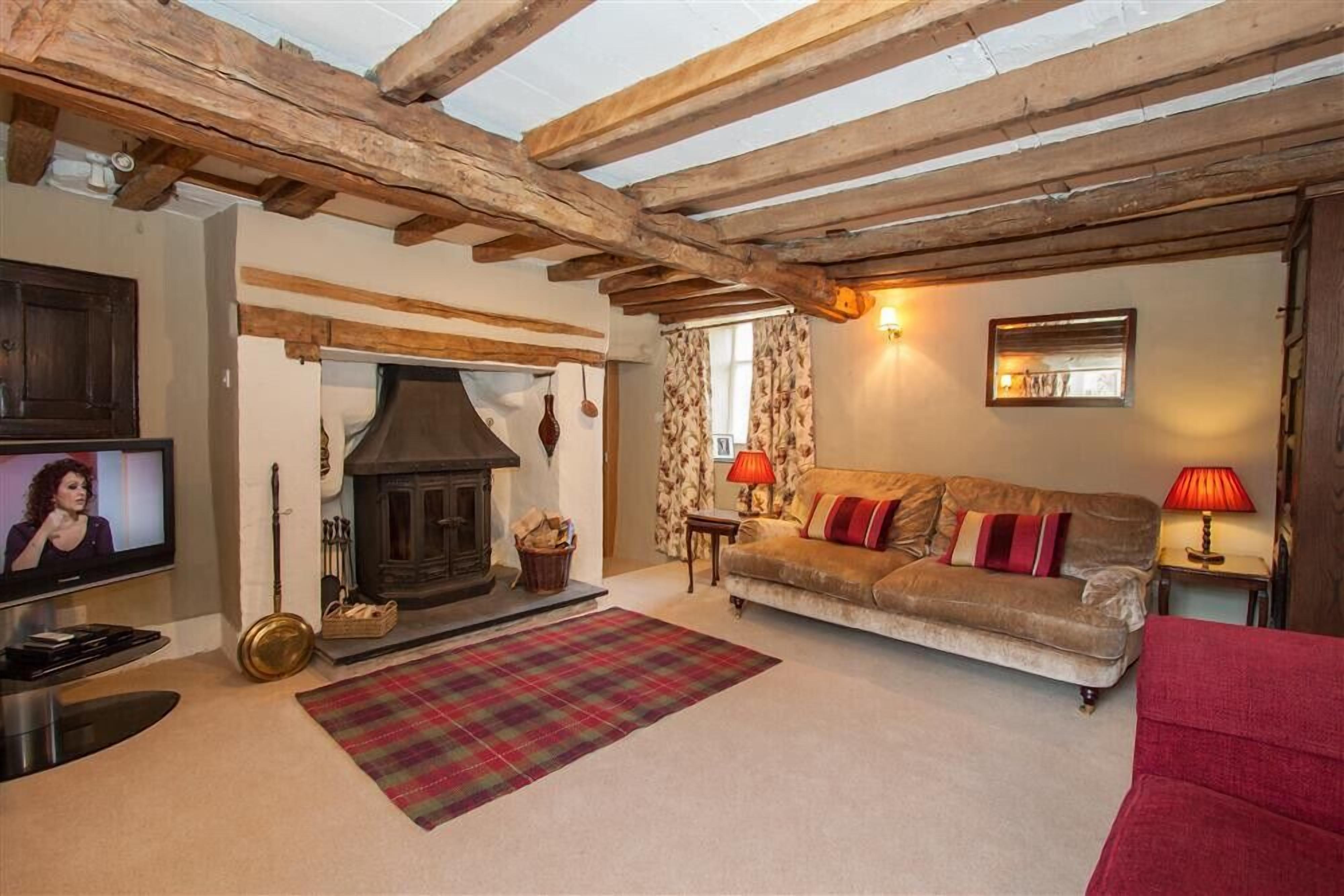 A cozy living room with exposed wooden beams, a fireplace, a sofa, and a television.