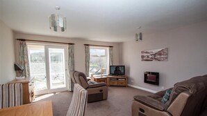 A living room with a sofa, armchair, and TV, large windows, and a painting on the wall. - Mellbreak (Ambleside)