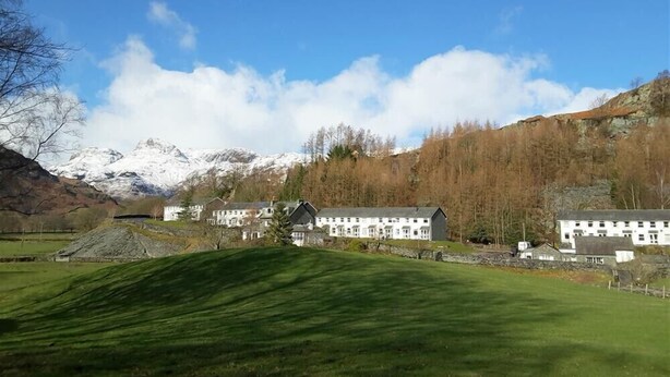 A hotel with multiple white buildings, a grassy foreground, and a backdrop of snow-capped mountains. - Mellbreak (Ambleside)