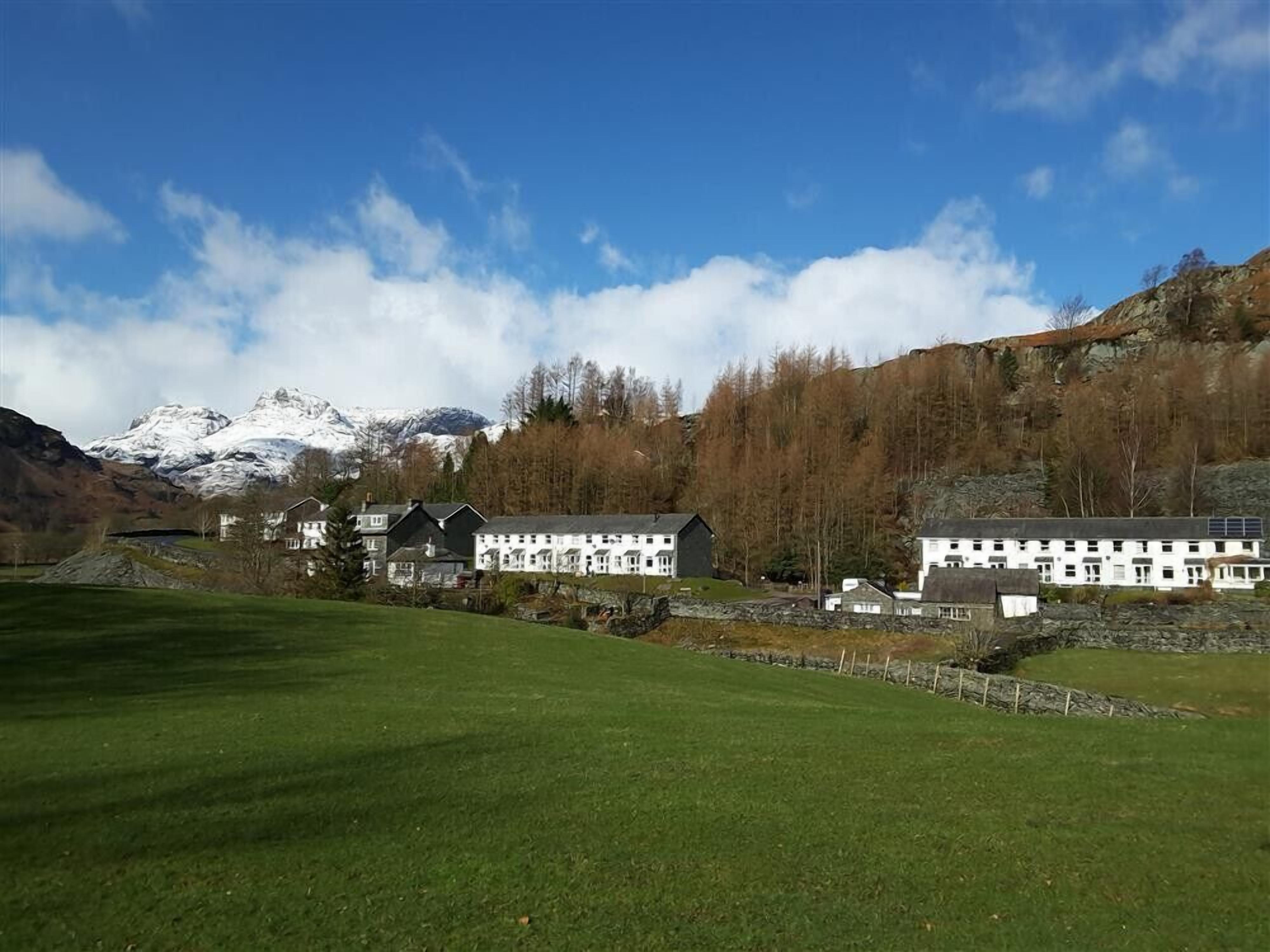 A hotel with multiple white buildings, a green field, and a mountain in the background.