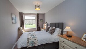 A bedroom with a bed, bedside table, lamp, and a window with curtains. - Mellbreak (Ambleside)