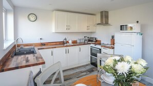 A modern kitchen with white cabinets, a wooden countertop, a microwave, a kettle, and a stove. - Oscar's Pad (Llanfairpwllgwyngyll)