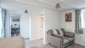 A cozy living room with a grey sofa, a small ottoman, and a dining area with a table and chairs. - Oscar's Pad (Llanfairpwllgwyngyll)