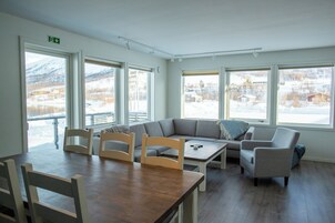Quarto com mesa de madeira, duas cadeiras, sofá cinza e janela com vista para a neve.