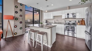 A modern kitchen with white cabinets, a large island with bar stools, a stainless steel refrigerator, and a view of the city through large windows.