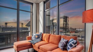 A modern living room with a large window offering a view of a bridge and construction cranes.