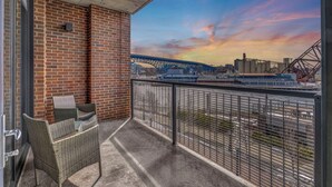 A balcony with wicker furniture, a brick wall, and a view of a bridge and industrial area.