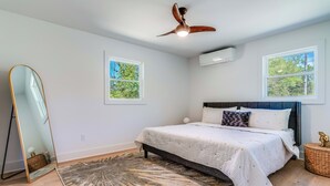 A bedroom with a bed, a standing mirror, a ceiling fan, and two windows. - New Paltz Modern Zen Cabin (New Paltz)