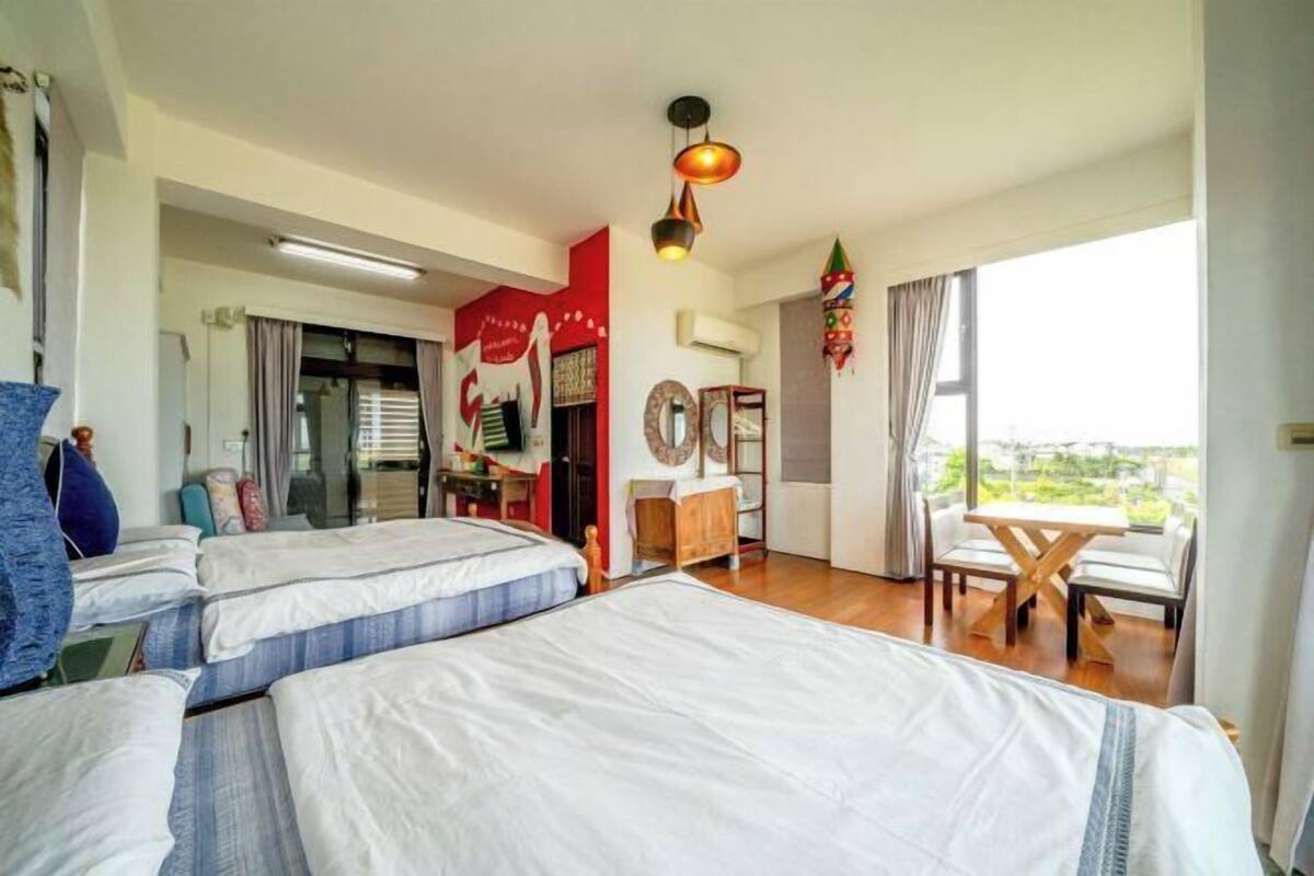 Habitación de hotel con dos camas, una mesa de comedor, un balcón y una pared roja con un cartel.